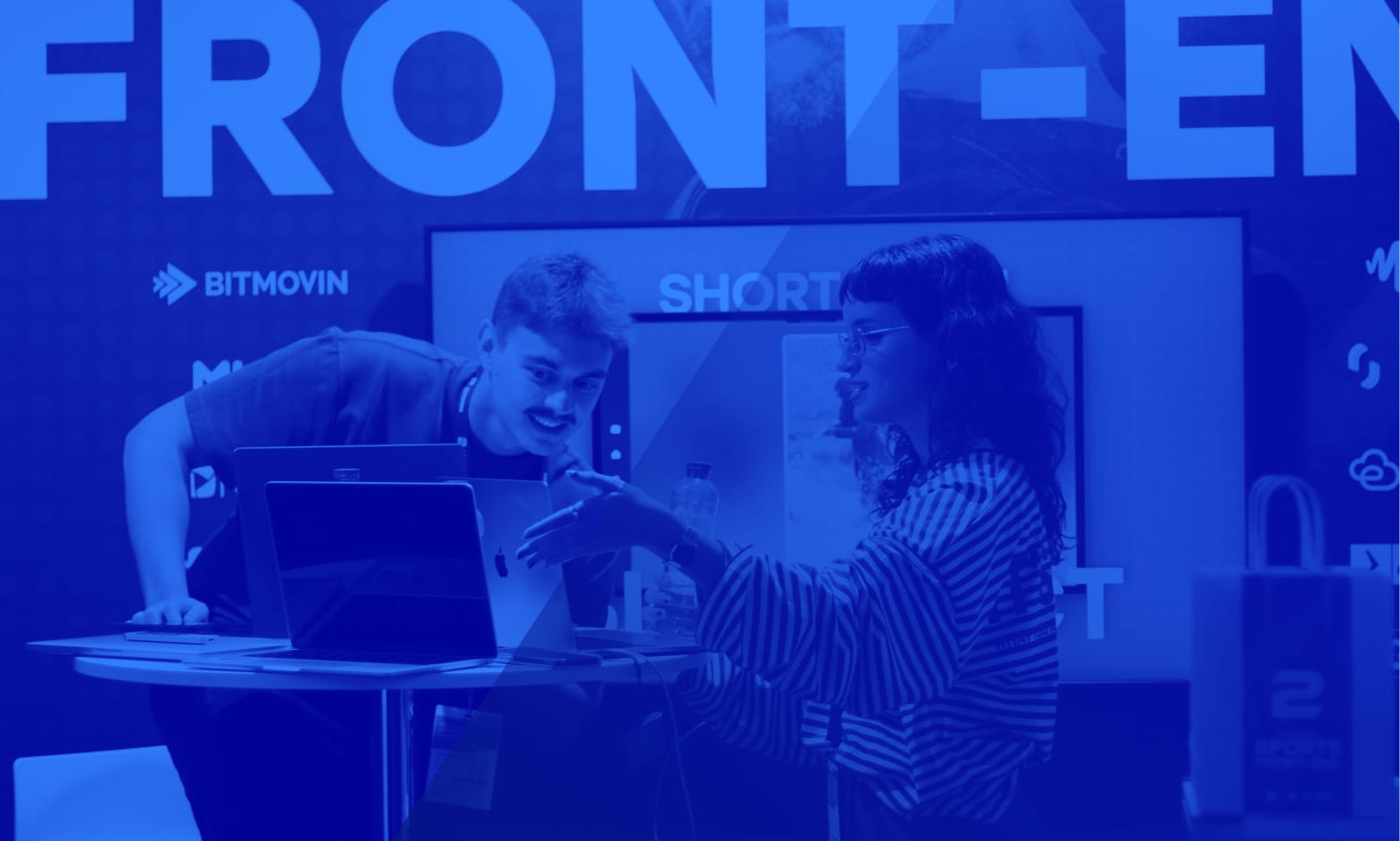Dos personas del equipo de 2Coders enseñando un desarrollo front-end en sus portátiles en el stand
