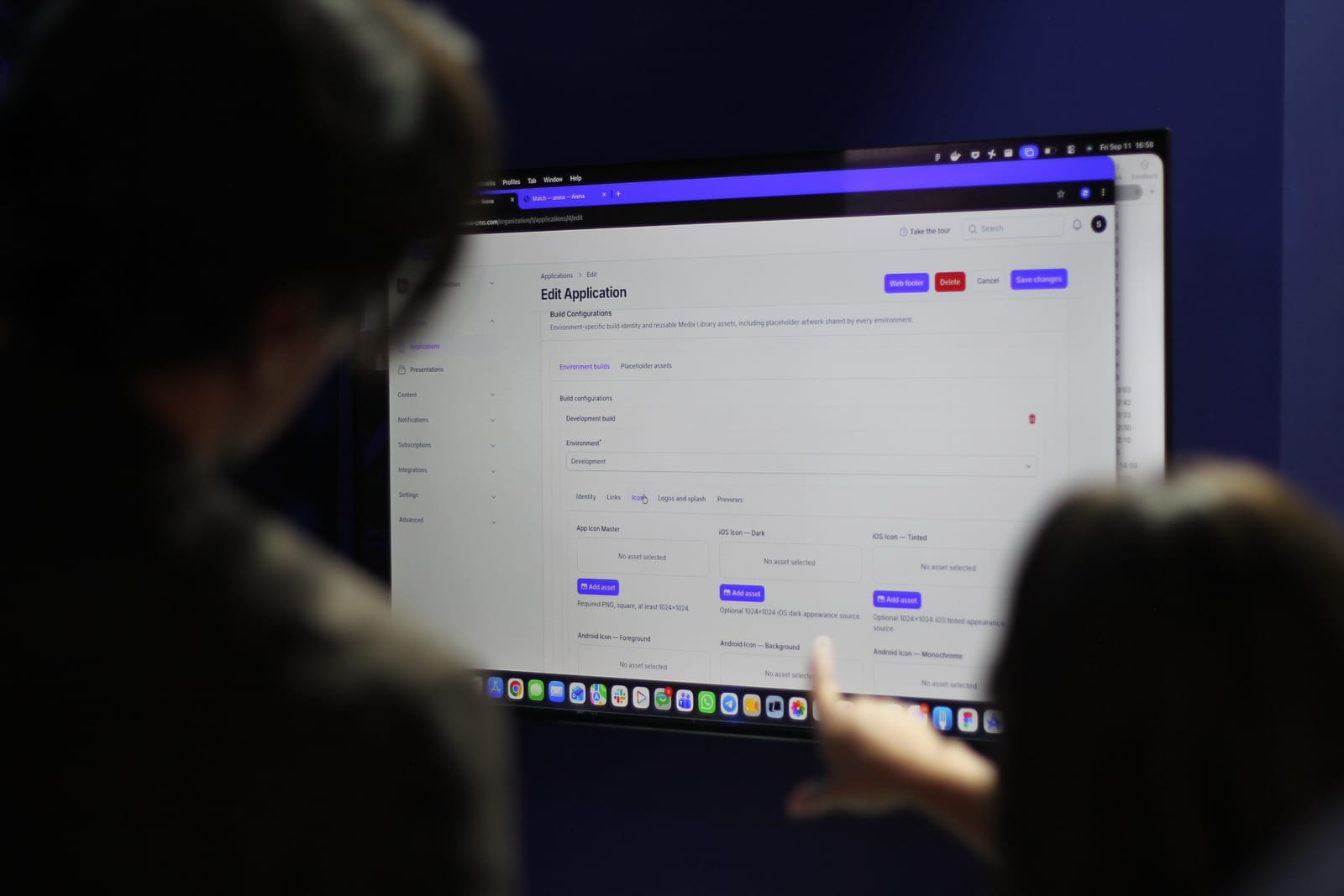 Due persone allo stand guardano il CMS di Arena su un portatile, sulla schermata Edit Application con le configurazioni di build e le icone dell'app.