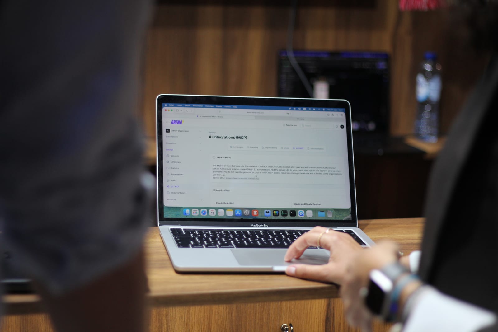 Un portatile sullo stand con le impostazioni delle integrazioni AI di Arena, l'URL del server MCP e le opzioni per collegare un assistente AI come client.