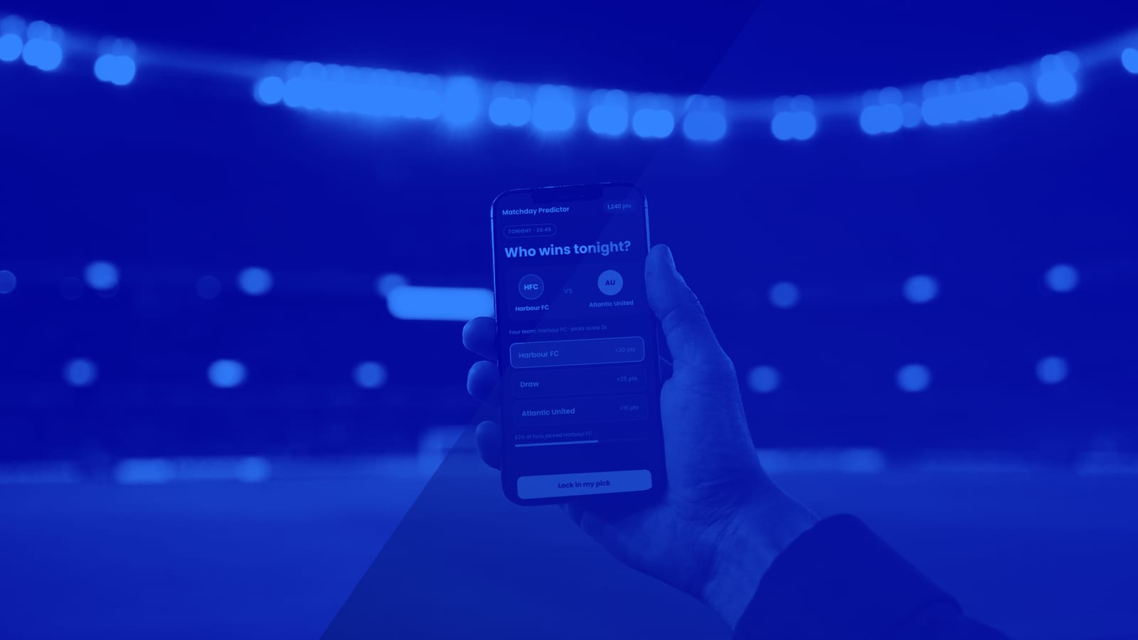 Un fan sostiene un móvil con un juego de predicción que pregunta «¿Quién gana esta noche?» en un estadio iluminado por los focos
